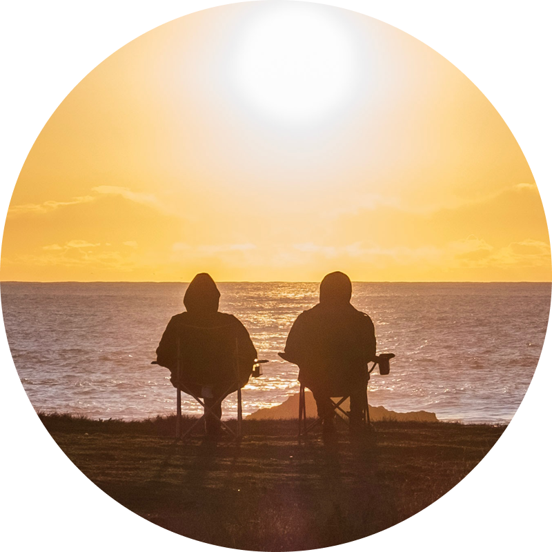 Two people sit watching the sunset over the ocean